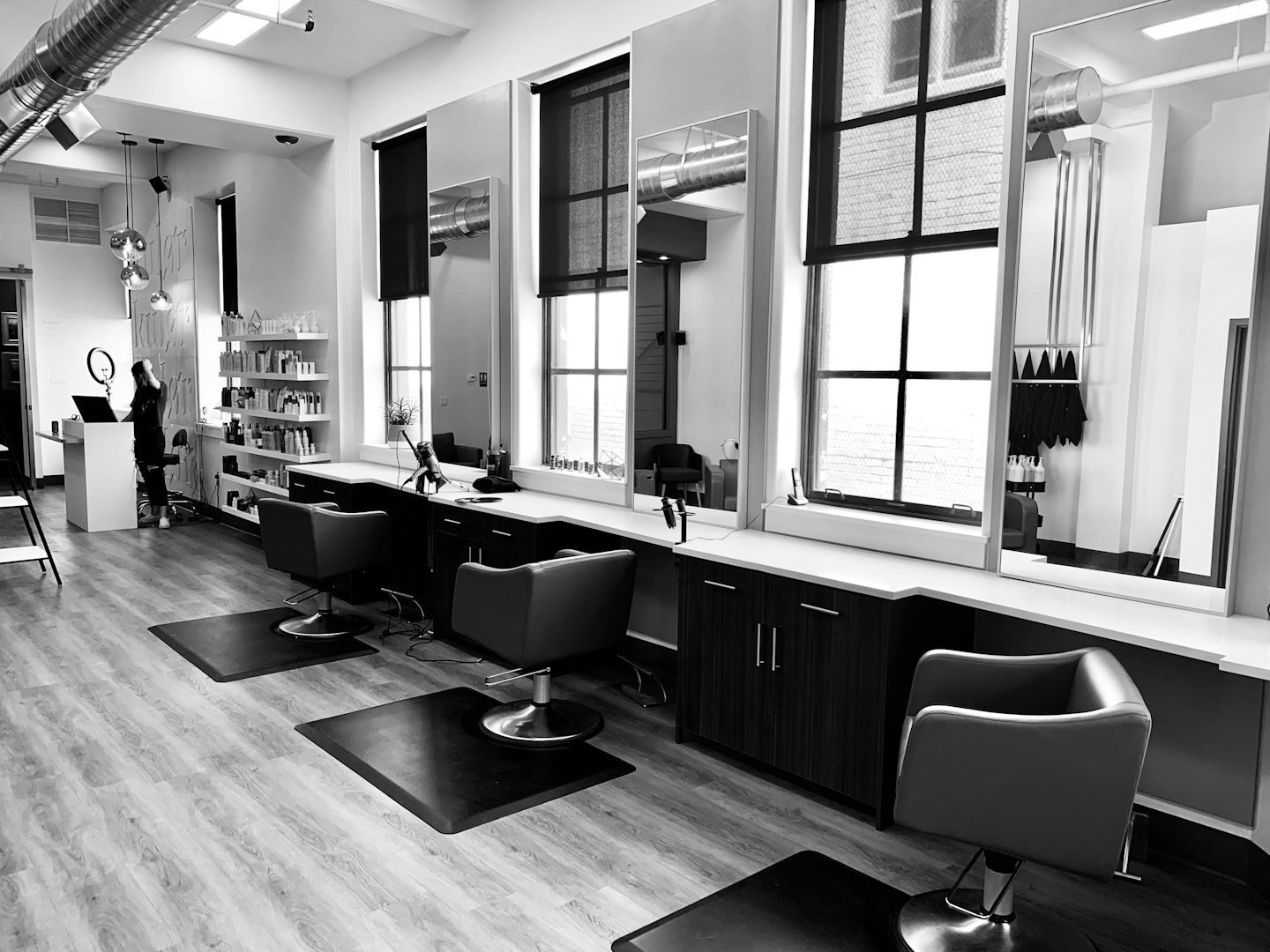 Nowoczesne salon fryzjerski ze stanowiskami do stylizacji i osobą przy ladzie.